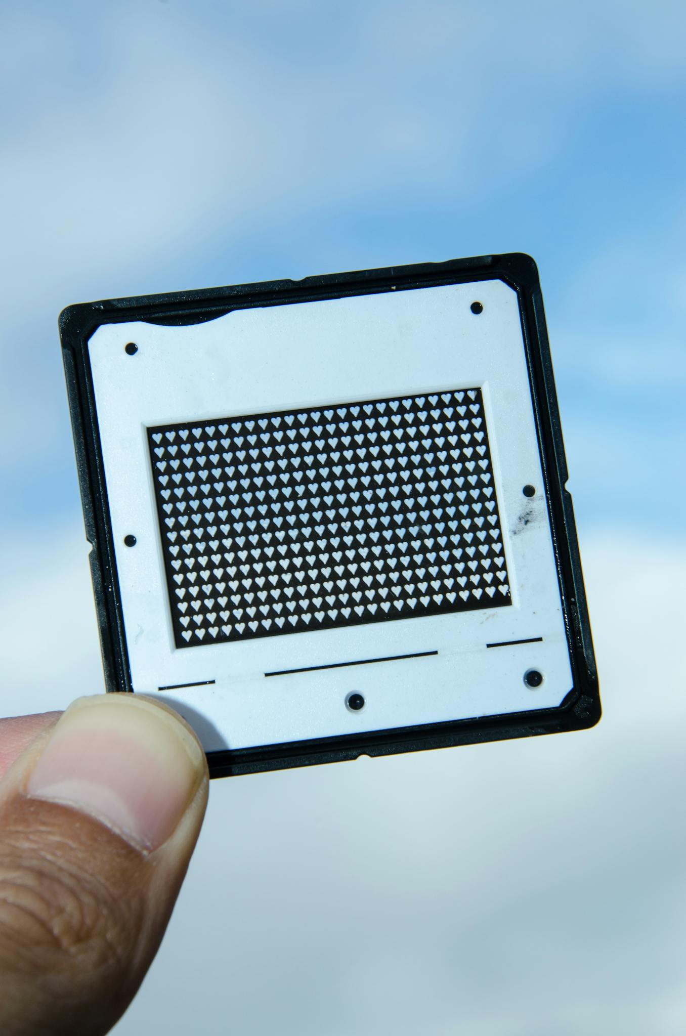 Close-up of a computer chip against a blue sky background, held by hand.