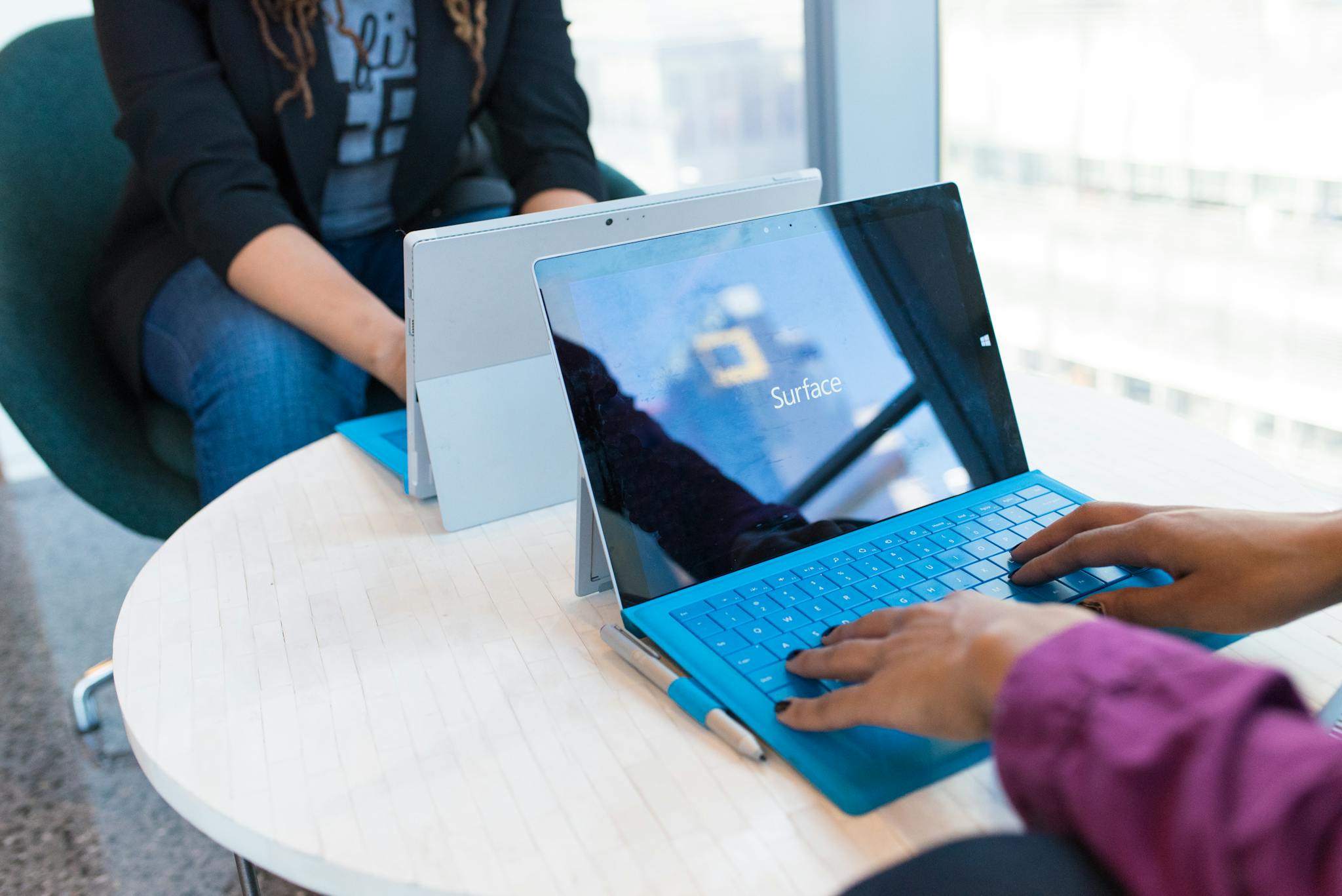 Two people using modern laptops in a bright office setting, showcasing technology in use.